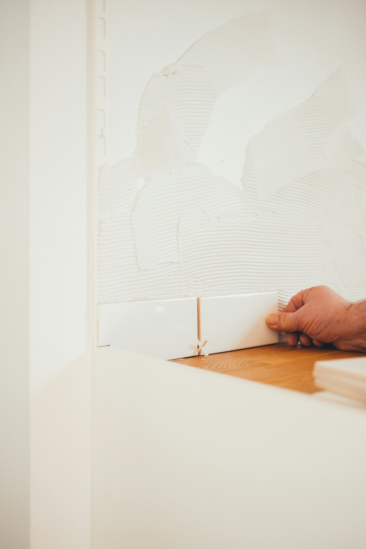 A tiler's hands holding a white ceramic tile before setting it.