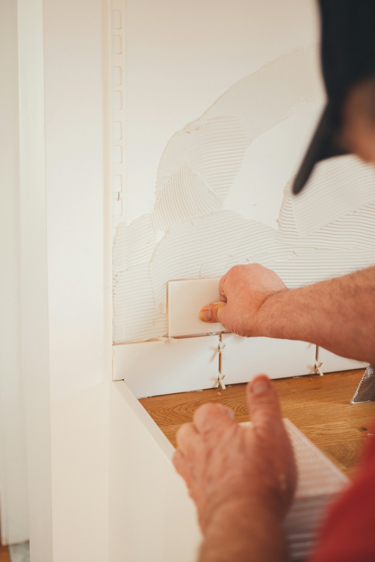 A tiler's hands pressing a tile firmly onto a prepared wall.
