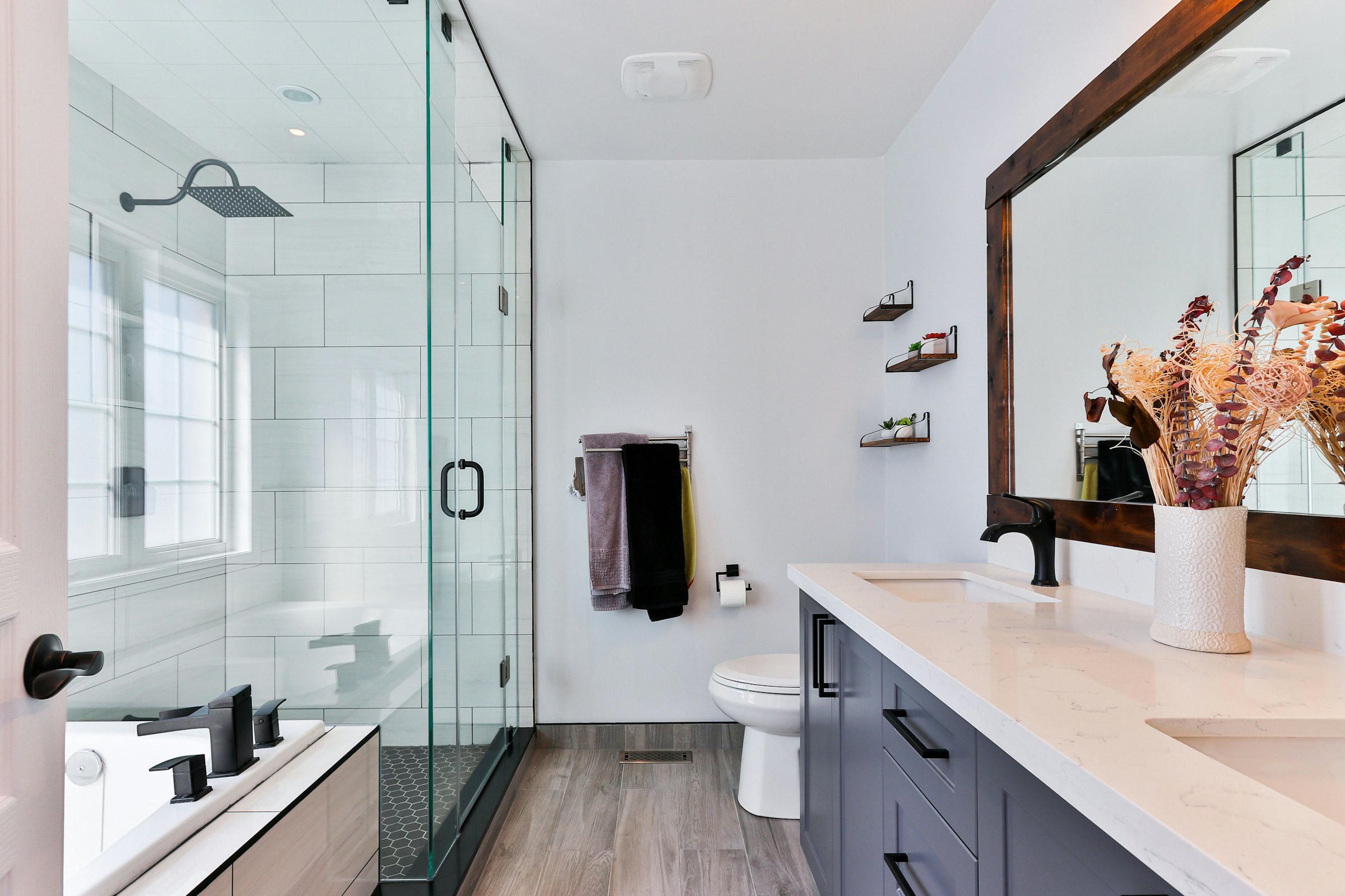 Finished main bathroom in Mosman: a walk-in glass shower, dark timber-framed mirror above twin basins on a stone benchtop, matte black tapware and timber-look flooring.